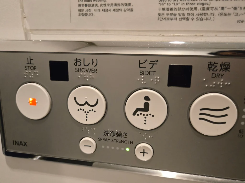 Japanese toilet control panel with pictograms, English labels, and braille for shower, bidet, dry, and stop buttons