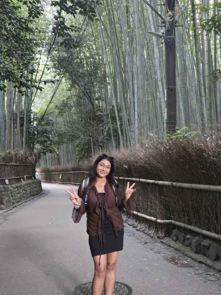 Nikita posing with victory signs on each hand, standing against the backdrop of Arashiyama Bamboo forest.
