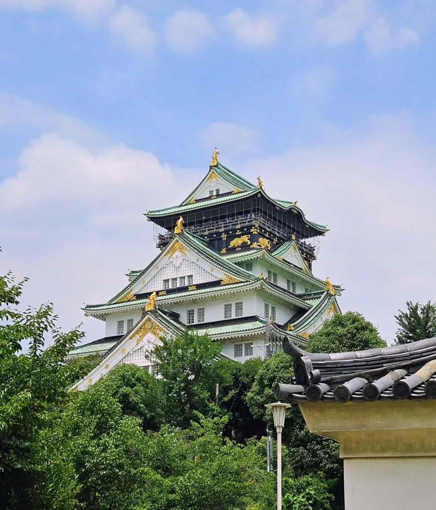 Osaka Castle's gold-trimmed tower rising above green trees under a blue sky